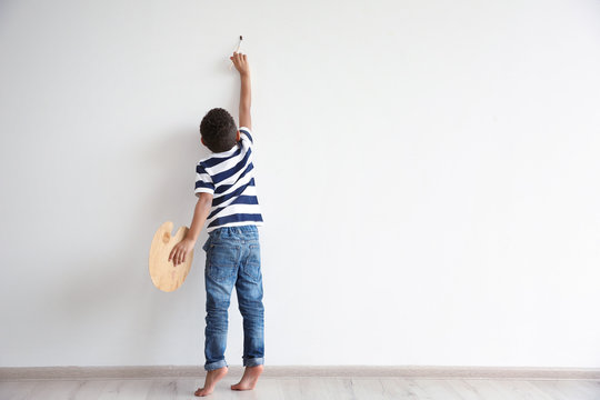 Little African-American boy painting on wall indoors