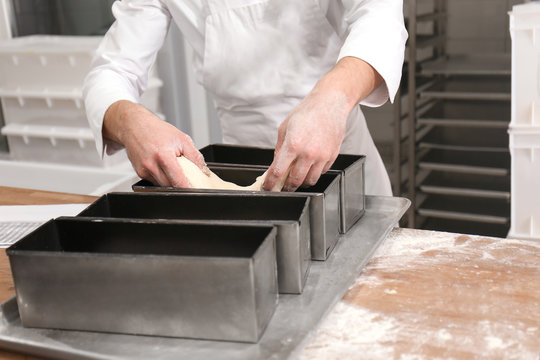 Man putting dough into metal form on table in bakery