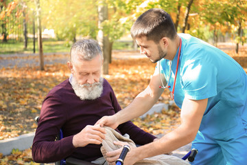 Young caregiver walking with senior man in park