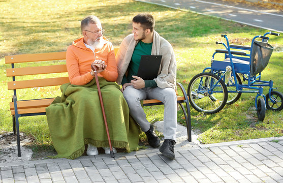 Young caregiver sitting with senior man on bench in park