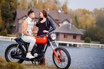 Plakat stylish and trendy couple in love on a motorcycle flirting close-up on a background of late autumn in the park