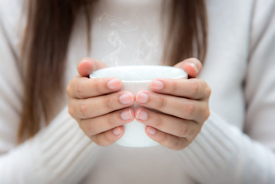 Woman's hand holding a white cup of coffee in winter season. With a beautiful winter manicure in sunny day.  Lifestyle Concept.