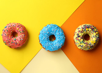 Tasty donuts with sprinkles on color background