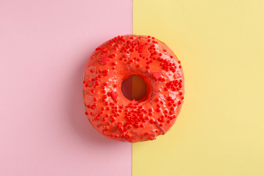 Delicious red donut on color background, top view