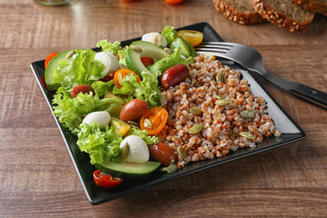 Plate with buckwheat porridge and fresh salad on table