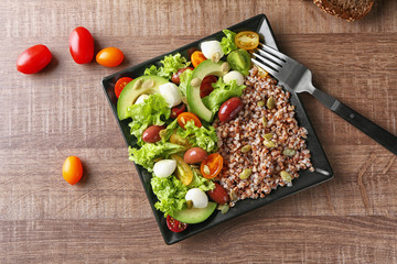 Plate with buckwheat porridge and fresh salad on table, top view