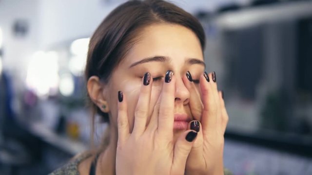 Makeup artist applies concealer on the face of a young girl using her hands. She is also doing massage. Base for perfect makeup. Slowmotion shot