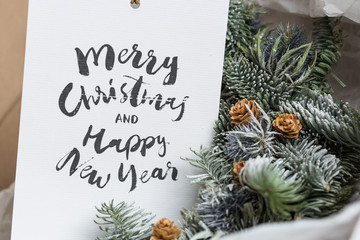 polygraphy, winter, holidays concept. very textured white card with words of greeting with christmas and new year, it is placed by spruce branches and pinecones
