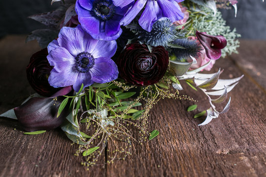growing, decoration, romance concept. on the wooden table there is adorable bouquet of flowers, wonderful maroon battercup is surrounded with lilac abemons