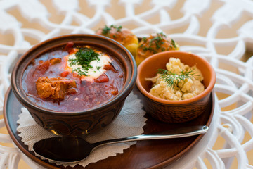 Ukrainian national cuisine, red borsch with meat and sour cream on a tray with lard and garlic dumplings