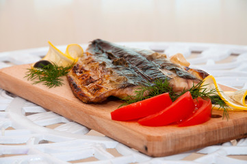 Grilled fish on a wooden board with lemon and tomatoes