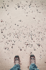 Person in hiking shoes stands on a beach, seen from above, color toned picture.