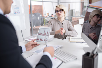 Portrait of successful blonde businesswoman discussing statistics report with colleague looking at graphs and charts with financial data during meeting in modern office