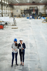 High angle view of confident inspector in formalwear taking necessary notes while young technician with blueprint in hands giving tour of modern factory