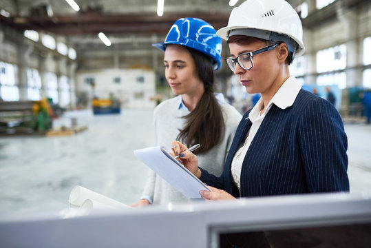 Carrying out inspection at modern plant: group of confident inspectors wearing hardhats standing at production department and taking necessary notes