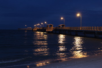 Fishing pier jetty along the shoreline with starburst lights on a water reflection