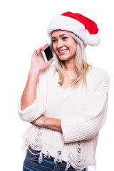 Portrait of a lovely smiling girl dressed in red christmas hat talking on mobile phone while standing and looking away at copy space isolated over white background