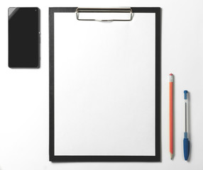 Blank clipboard, smartphone, pen and pencil on white background.
