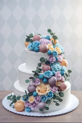 Beautiful three-tiered white wedding cake decorated with colorful flowers roses. Concept of elegant holiday desserts