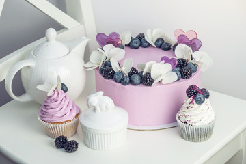 Purple beautiful cake decorated with berries, blackberries and blueberries on top with cupcakes on the festive table