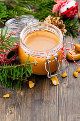 Obraz na płótnie Canvas Homemade salted caramel sauce in a glass jar and Christmas decor on wooden background