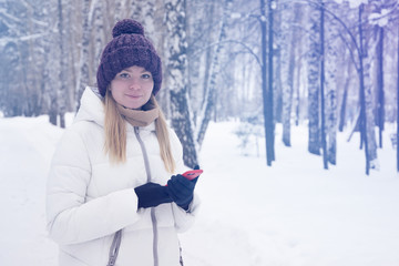 Fototapeta na wymiar girl in a winter forest with a fashionable modern mobile phone (smartphone) in special gloves for working with a touch screen
