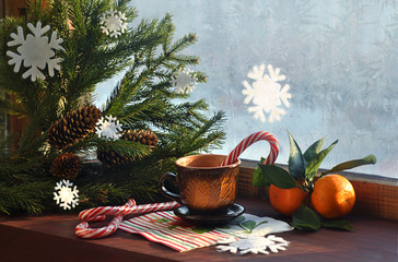 Snowy window and branches of the Christmas tree, hot drink, candy and tangerines. Christmas and New Year's card