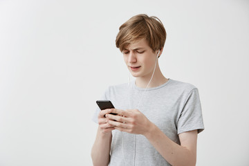 Fototapeta premium Shocked puzzled hipster guy messages with friends, uses free internet connection on modern cell phone, receives bad news. Astonished young male recieves bad news. Human feelings, emotions, reaction