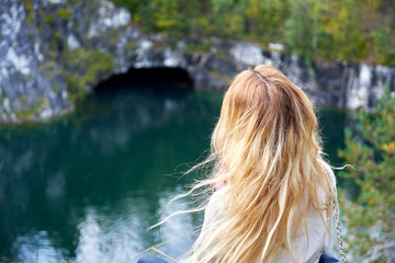 Young woman with long blonde hair enjoying beautiful lake view at a canyon while sitting on the ground.