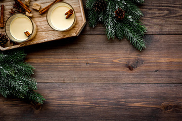 Winter attributes. Glasses of classic eggnog with spices near spruce branch on dark wooden background top view copyspace