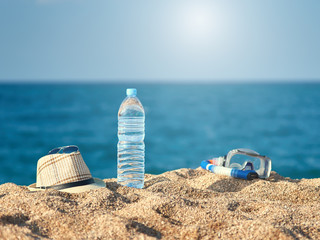 Beach accessories. Bottle of pure water, sunglasses, mask for swimming and men’s sunhat on the beach sand against the sea.