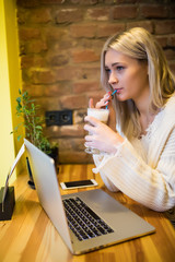 Beautiful blonde woman using laptop at cafe while drinking coffee, Relaxing holiday concept.