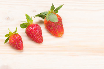 three ripe red strawberries lie on a wooden board