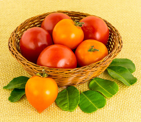 large red tomato in a wicker brown basket with a heart-shaped fruit with green leaves close-up - Powered by Adobe