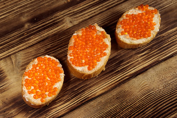Sandwiches with butter and red caviar on wooden table
