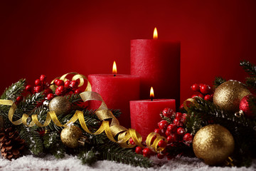 Christmas candle with fir-tree branches and baubles on red background
