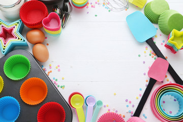 Empty cupcake cases with different kitchen utensils on white wooden table