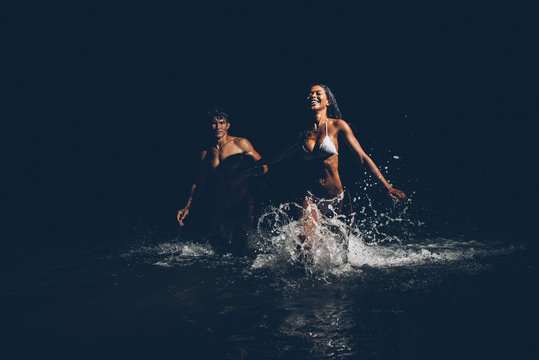 Young couple running in the ocean during the night bath