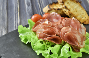 cold meat plate. Sliced ham with lettuce leaves on a dark stone background, selective focus