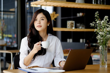 An attractive young businesswoman having coffee while working at coffee shop desk.