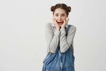 Young frightened woman in casual holding her hands on cheeks and screaming in panic. Schoolgirl being terrified after watching horror movie. Emotions concept