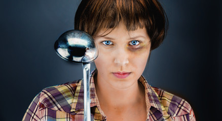 Woman with a bruise on her face and a ladle in her hand and an aggressor reflection on it