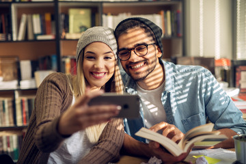 Motivated happy beautiful hipster love student couple taking a selfie in the sunny school library.