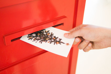 Hand dropping Christmas postcard into red mailbox sending Xmas wish to other people on seasonal...