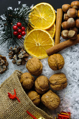 Winter abstract arrangement in studio on black background with snow, cinnamon sticks, lemon slices, frosty fir cone and braches and some small presents near a sack full of nuts.