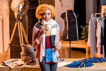 Portrait of a young african creative person with colorful scarf holding hot drink at the studio interior
