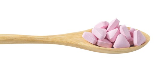 Wooden Spoon Full of Pink Vitamins on White