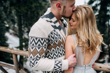 Beautiful young couple in the snowy forest, man is kissing woman in forehead