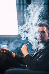 Man vaping fumes and drinking alcohol to relax. Unwinding pleasure and chilling concept