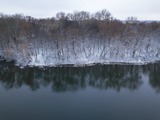 View from height to the winter forest covered with snow and standing on the river bank